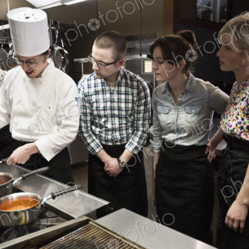 A chef and students at a cookery class in a commercial kitchen A chef and students at a cookery class in a commercial kitchen
