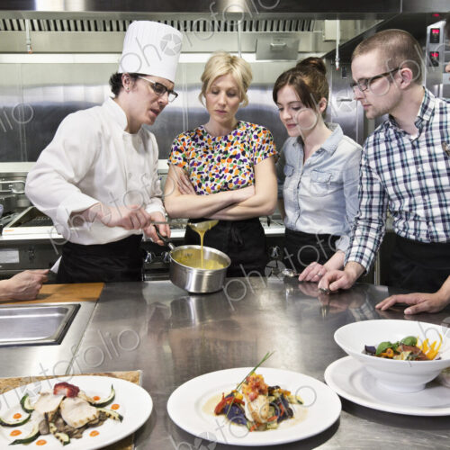 A chef and students at a cookery class in a commercial kitchen A chef and students at a cookery class in a commercial kitchen