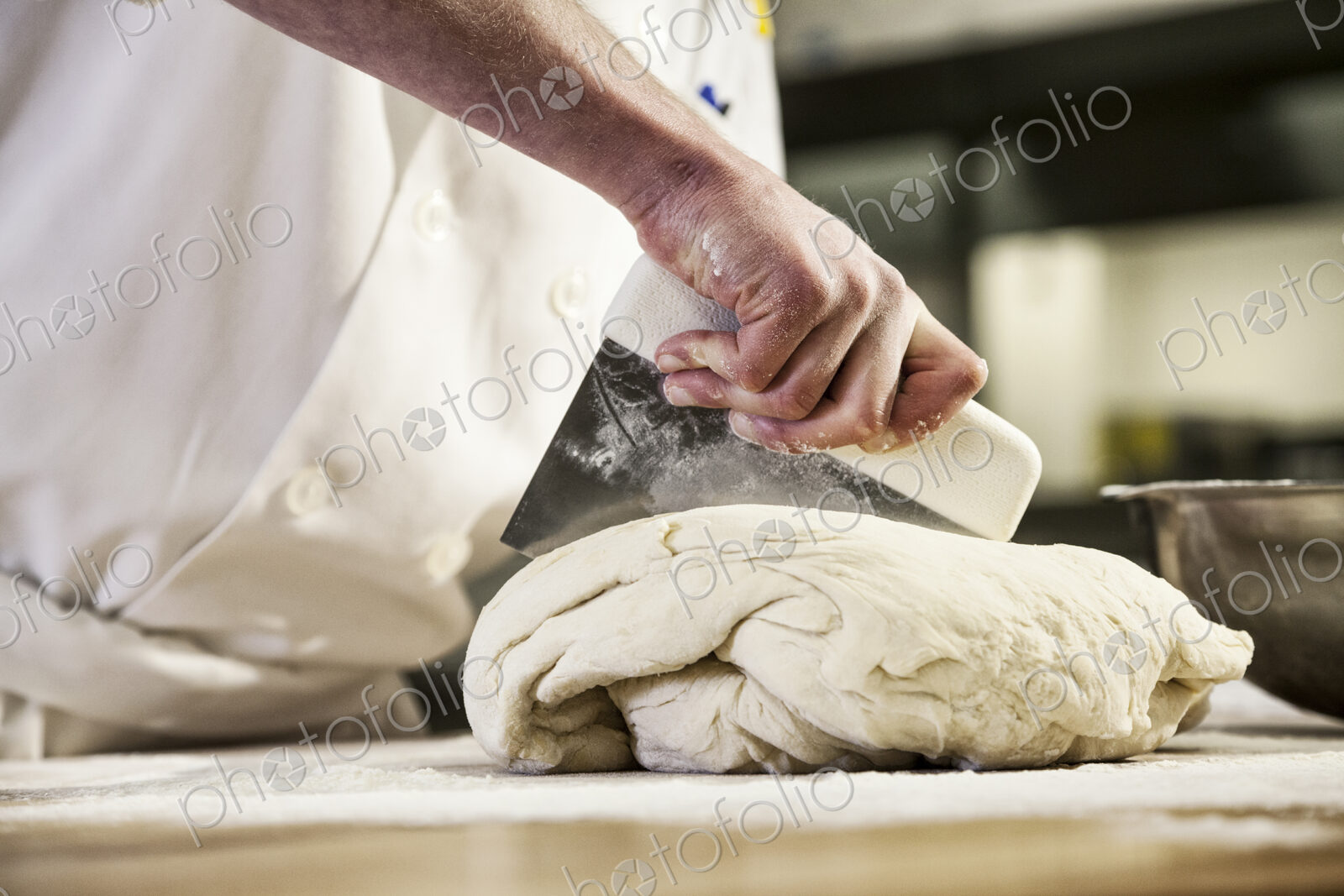 A chef dividing up bread dough into sections on a floured worktop.