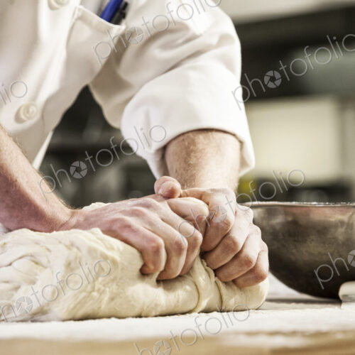 A chef's hands kneading bread dough on a floured worktop.