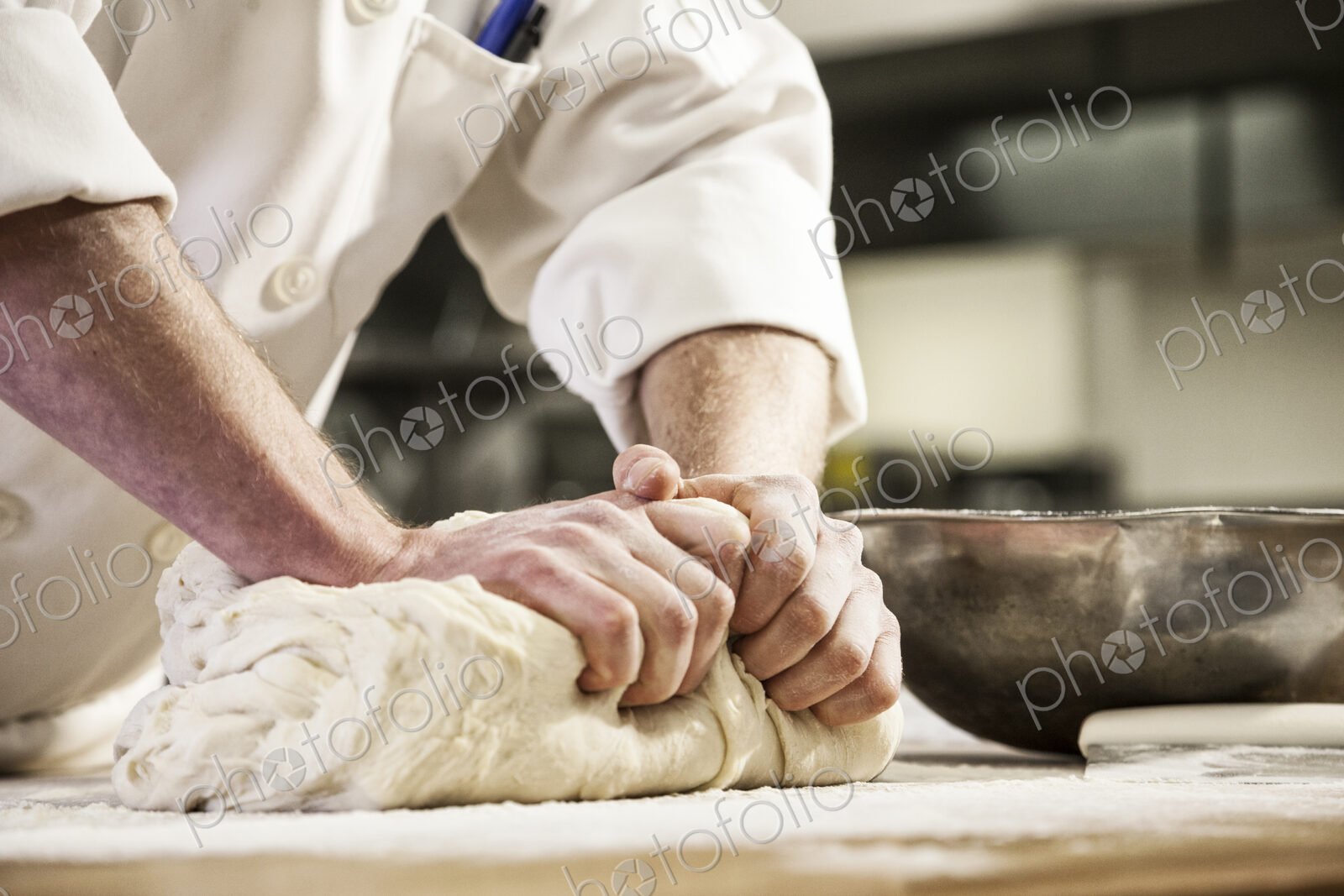 A chef’s hands kneading bread dough on a floured worktop.