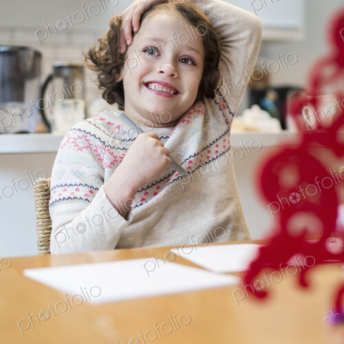 A child, a girl sitting at a table at home, drawing and writing cards before Christmas.