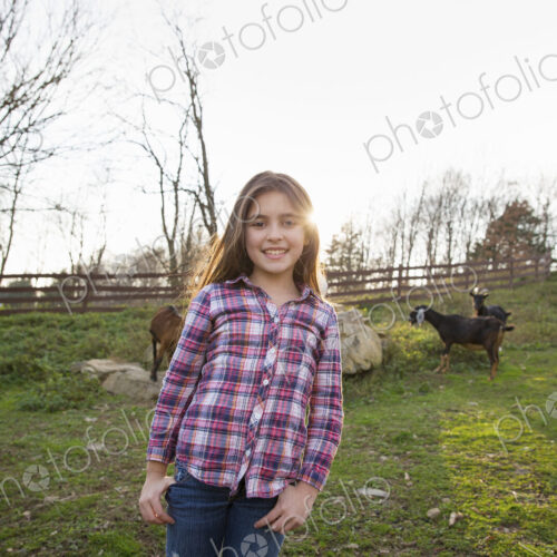 A child, a young girl in the goat paddock enclosure at an animal sanctuary.