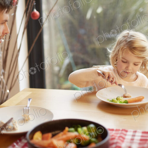 A child and a man sitting at a table eating a cooked meal.