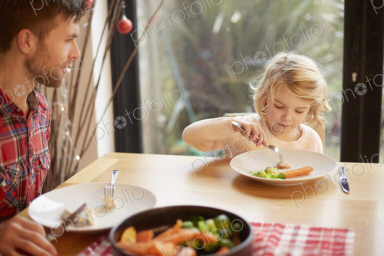 A child and a man sitting at a table eating a cooked meal.
