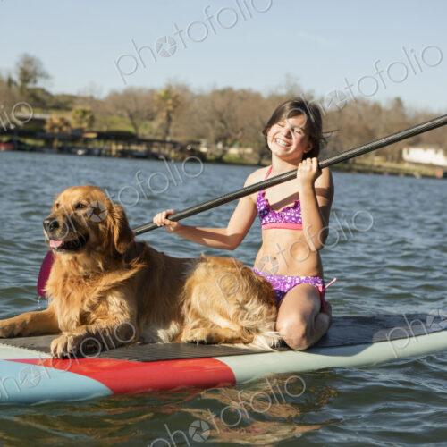 A child and a retriever dog on a paddleboard on the water.