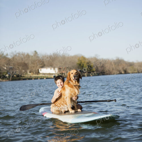 A child and a retriever dog sitting on a paddleboard on the water.