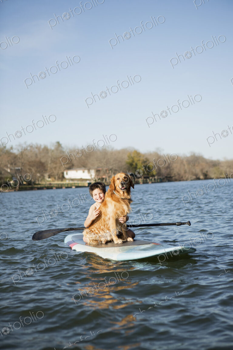 A child and a retriever dog sitting on a paddleboard on the water.