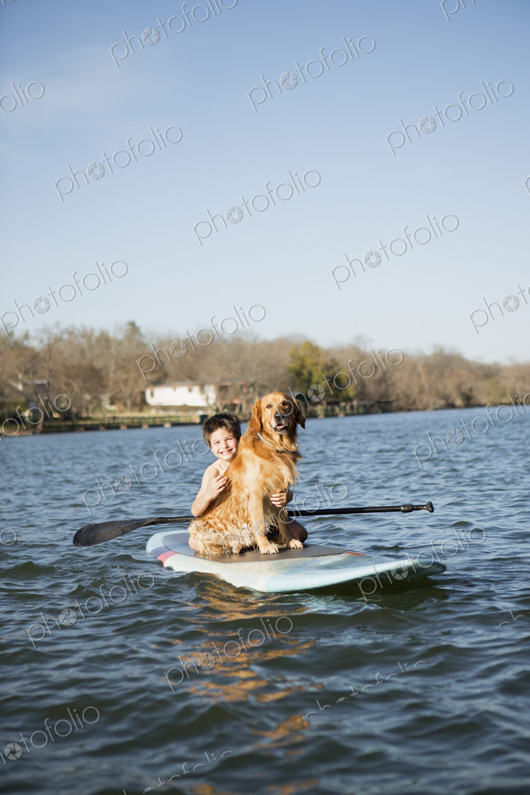 A child and a retriever dog sitting on a paddleboard on the water.