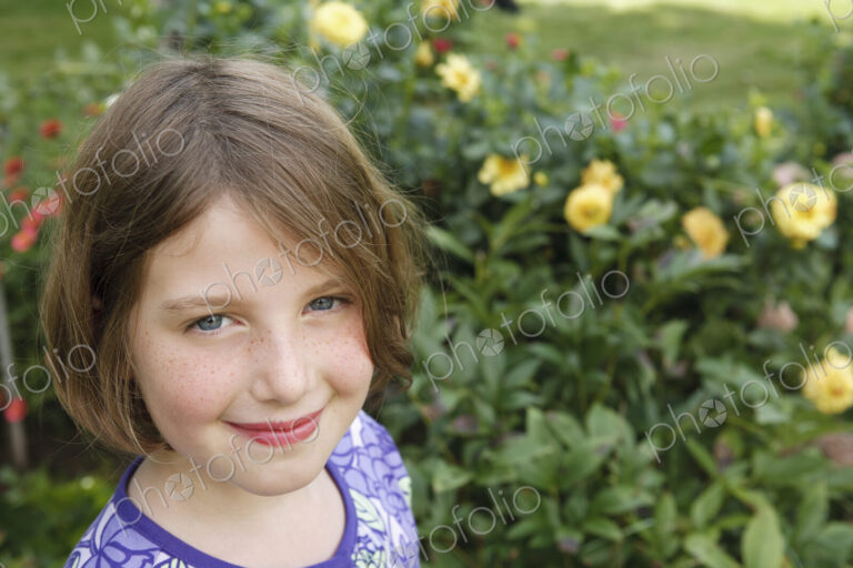 A child in a garden looking up and smiling.