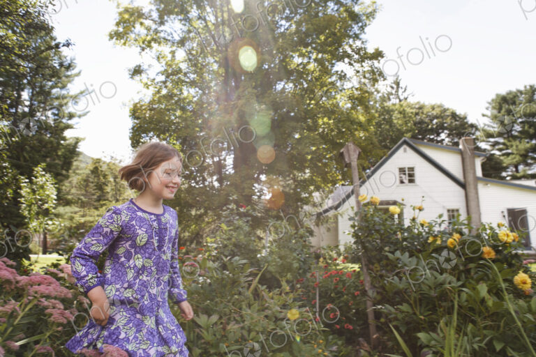 A child in a patterned blue dress running through a house garden.