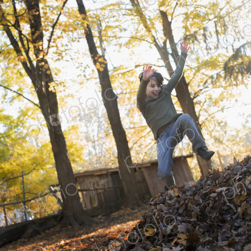 A child in autumn sunshine in a woodland. Leaping into a large pile of raked up autumn… A child in autumn sunshine in a woodland. Leaping into a large pile of raked up autumn…