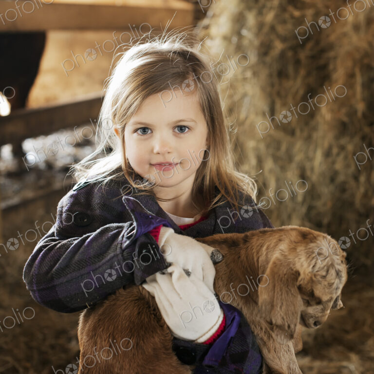 A child in the animal shed holding and stroking a baby goat.