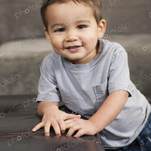 A child leaning on a brown chair, looking at the camera, smiling. A child leaning on a brown chair, looking at the camera, smiling.