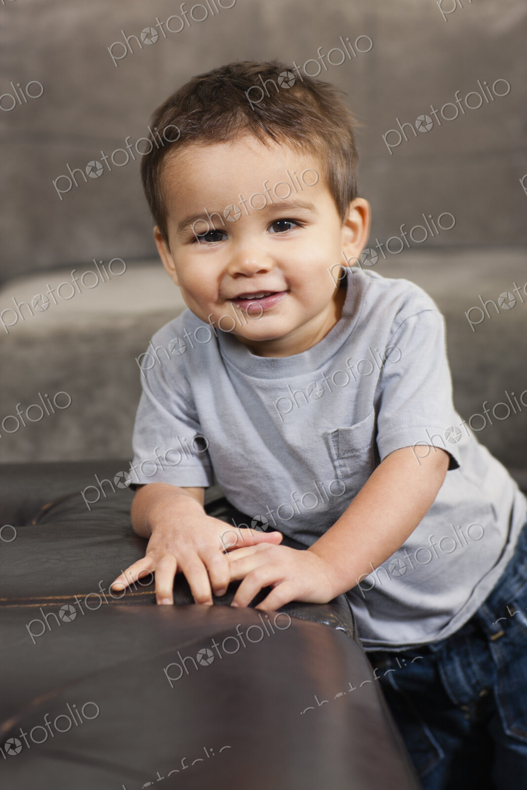 A child leaning on a brown chair, looking at the camera, smiling.