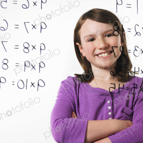 A child looking at a series of multiplication tables written on a see through surface.
