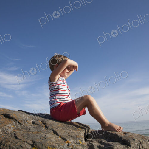 A child seated on the rocks looking out to sea.