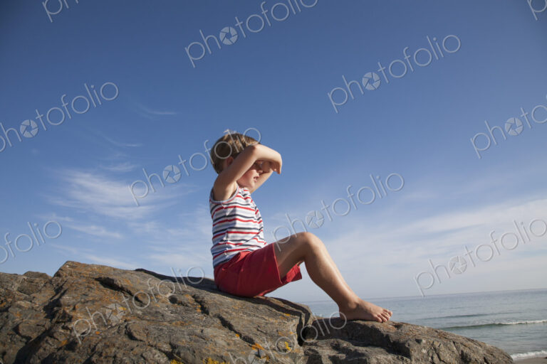 A child seated on the rocks looking out to sea.
