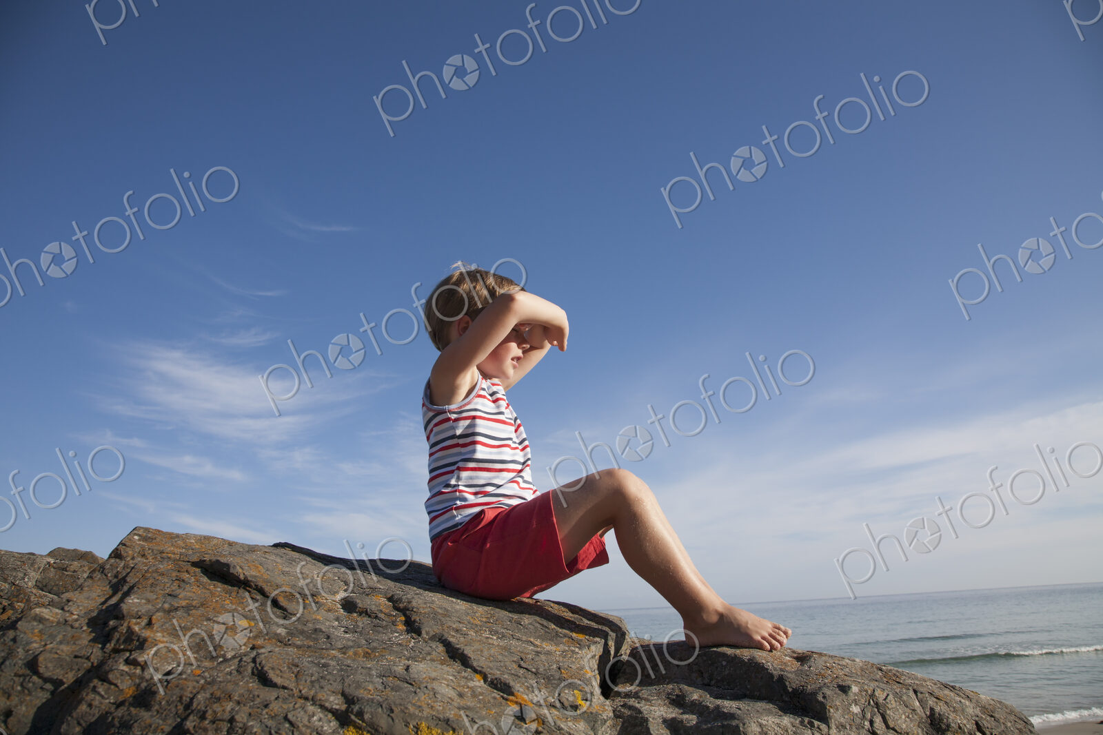A child seated on the rocks looking out to sea.