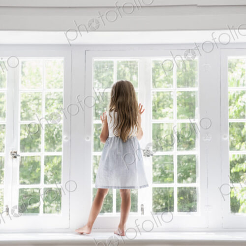 A child standing at a window looking out.