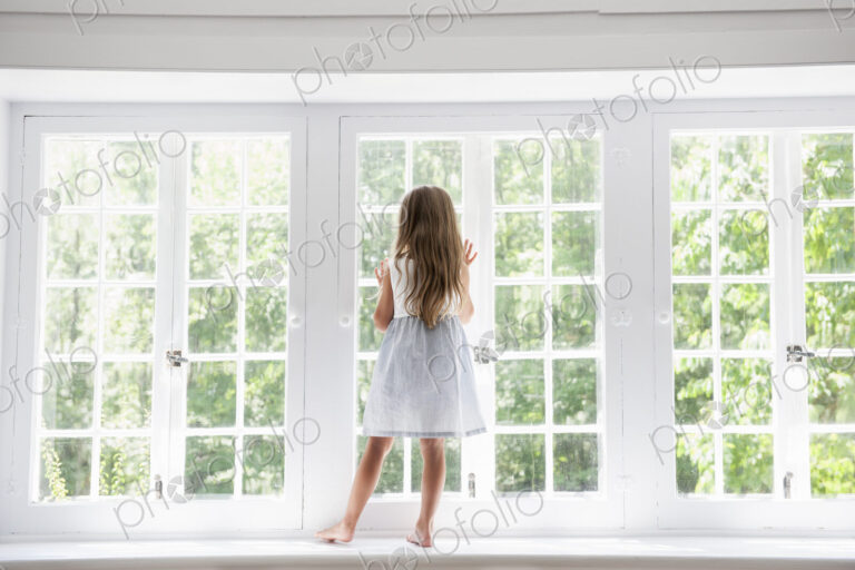 A child standing at a window looking out.