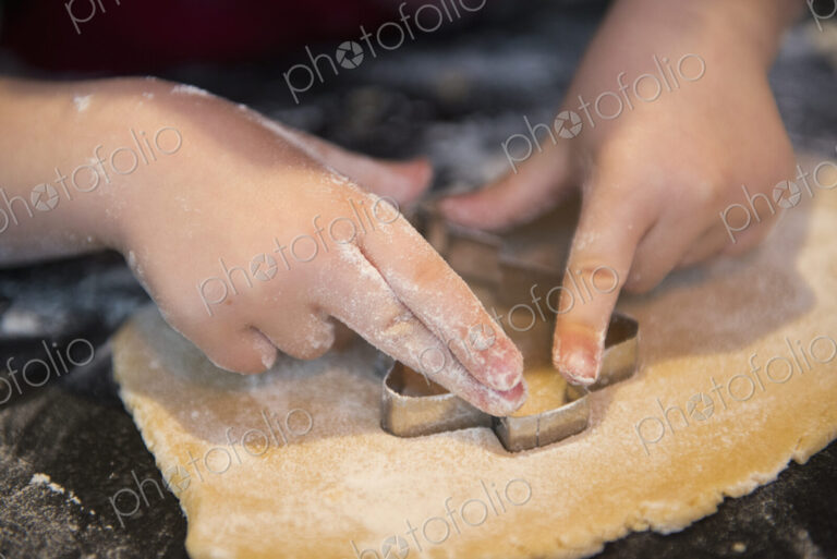 A child using a cookie cutter, making Christmas biscuits.