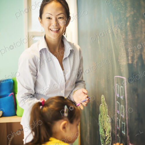 A child writing on the chalkboard and a teacher beside her.
