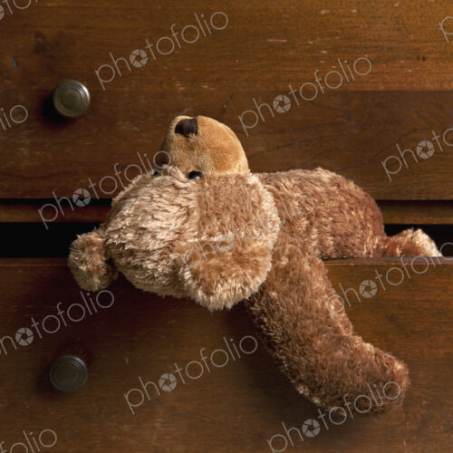 A children's brown soft toy teddy bear hanging out of a drawer. A children's brown soft toy teddy bear hanging out of a drawer.