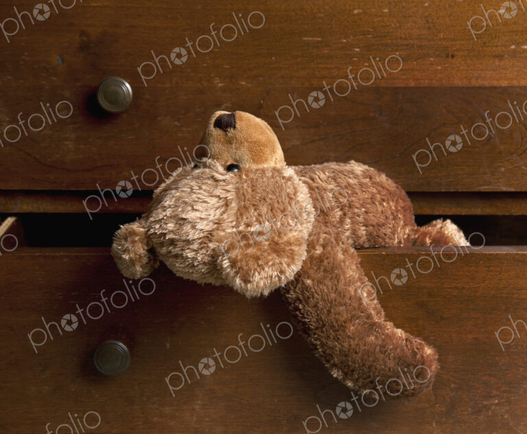 A children's brown soft toy teddy bear hanging out of a drawer.