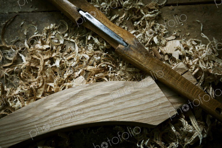 A chisel and wooden object with wood shavings, on a workbench.