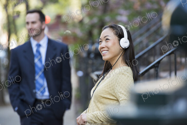 A city street with steps up to the brownstone buildings. A woman wearing music…