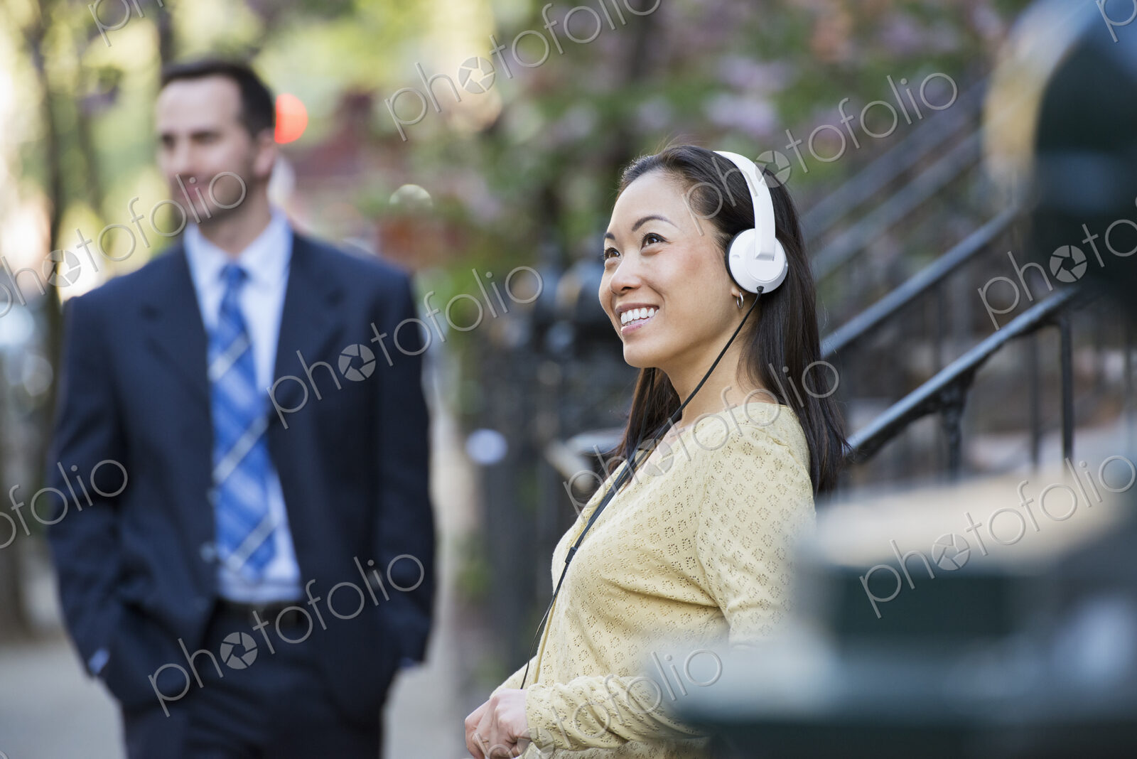 A city street with steps up to the brownstone buildings. A woman wearing music…