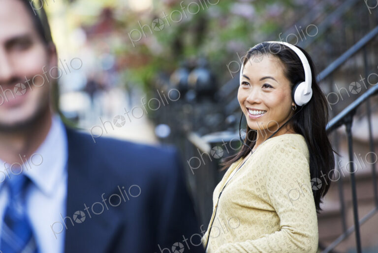 A city street with steps up to the brownstone buildings. A woman wearing music…