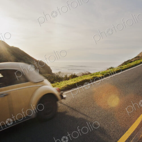 A classic car on a highway along the Pacific coast in the evening light in northern… A classic car on a highway along the Pacific coast in the evening light in northern…