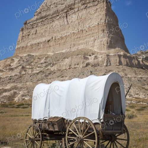 A classic covered wagon known as a prairie schooner, on open prairie below the…