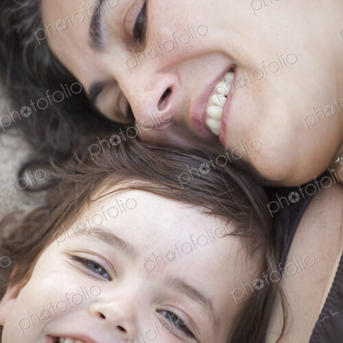 A close up of a mother and daughter lying with their heads together, smiling and laughing.