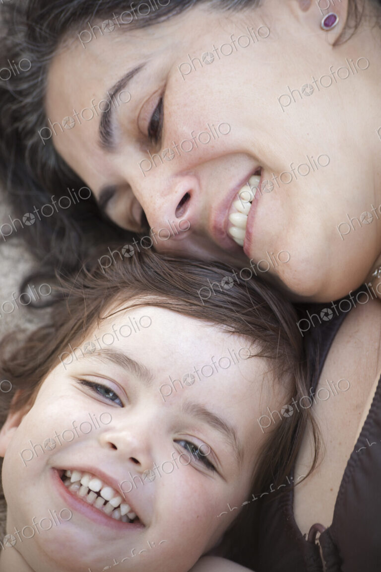 A close up of a mother and daughter lying with their heads together, smiling and laughing.