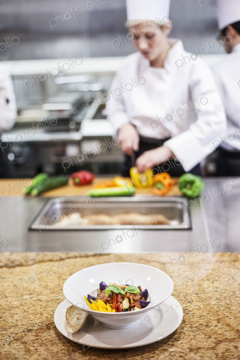 A closeup of a finished plate of food with chefs working in the background in a…