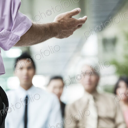 A closeup of a hand gesturing to a group of business people in a meeting. A closeup of a hand gesturing to a group of business people in a meeting.