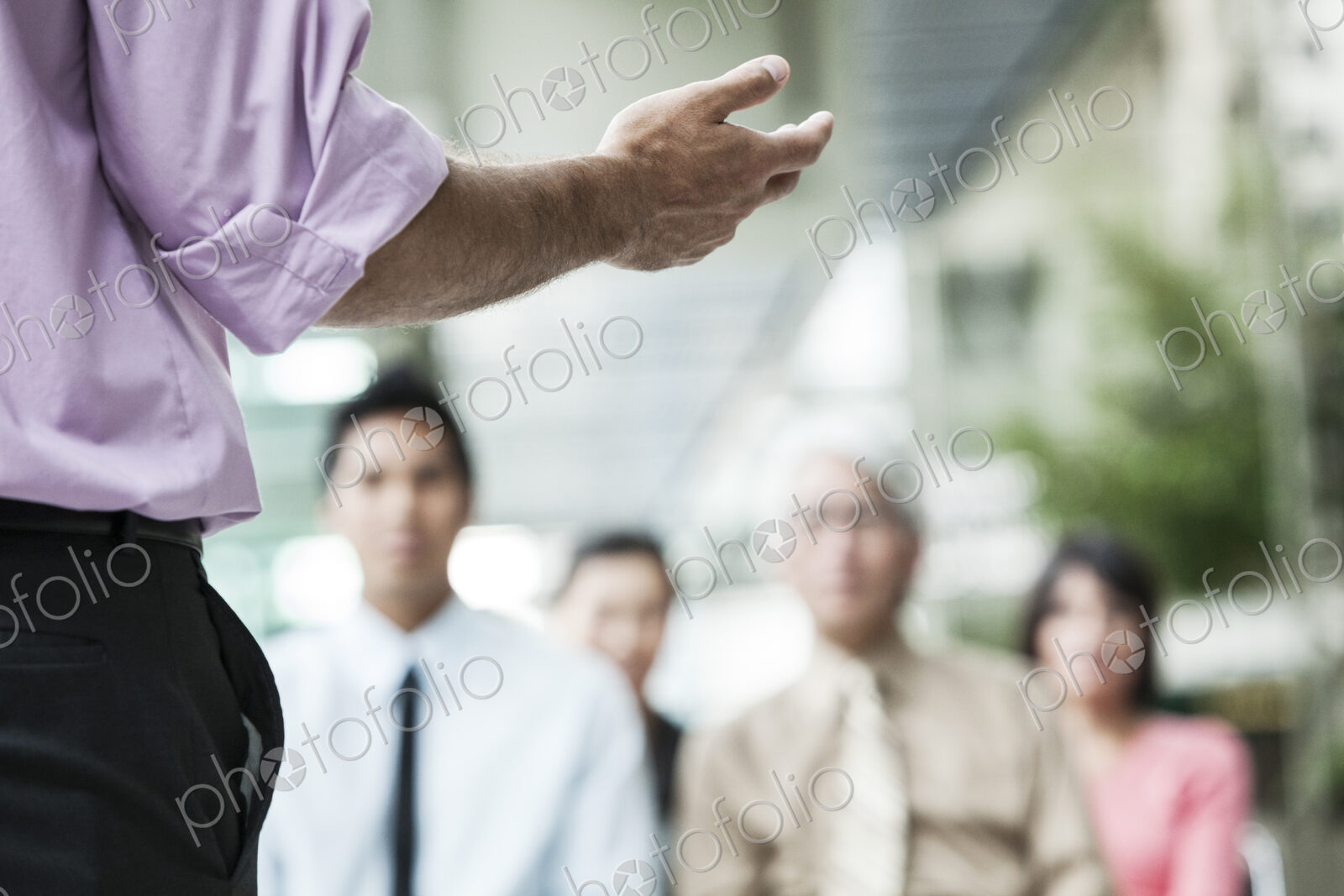 A closeup of a hand gesturing to a group of business people in a meeting.