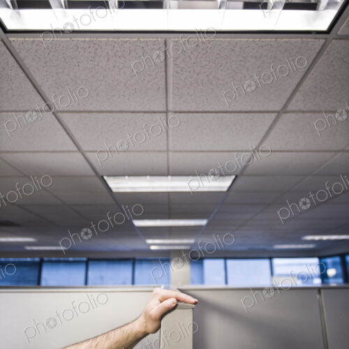 A closeup of a hand of a businessman resting on a wall between cubicles.