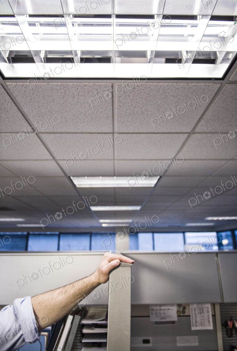A closeup of a hand of a businessman resting on a wall between cubicles.