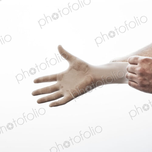 A closeup of a hand pulling on a medical examination glove. A closeup of a hand pulling on a medical examination glove.