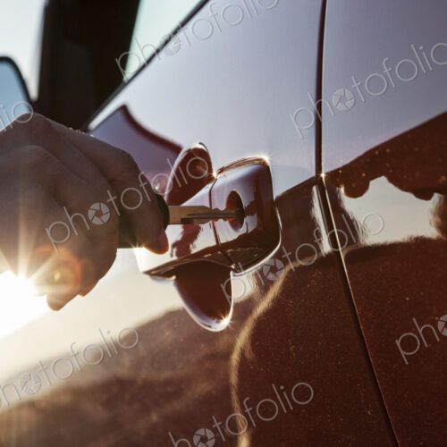 A closeup of a hand putting a key in the door of an automobile. A closeup of a hand putting a key in the door of an automobile.