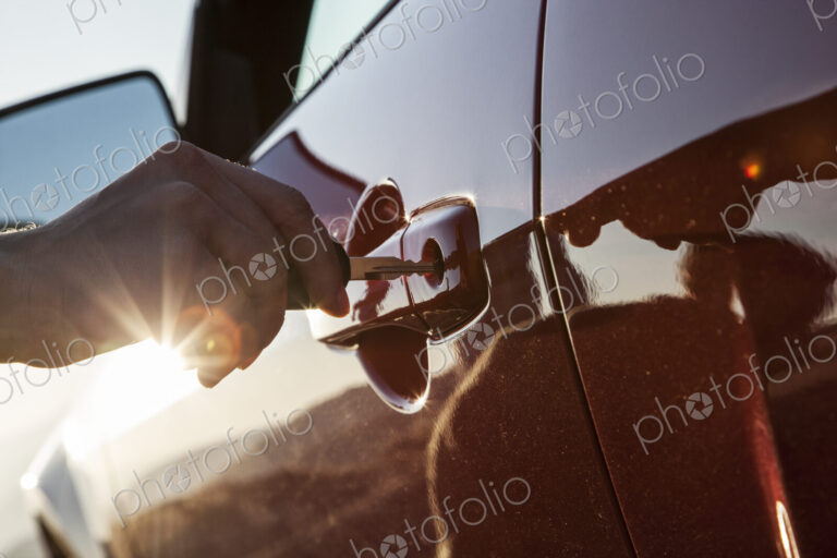 A closeup of a hand putting a key in the door of an automobile.