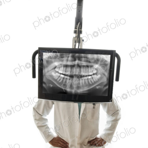 A closeup of a monitor with a dental x-ray and a dentist standing behind the monitor. A closeup of a monitor with a dental x-ray and a dentist standing behind the monitor.