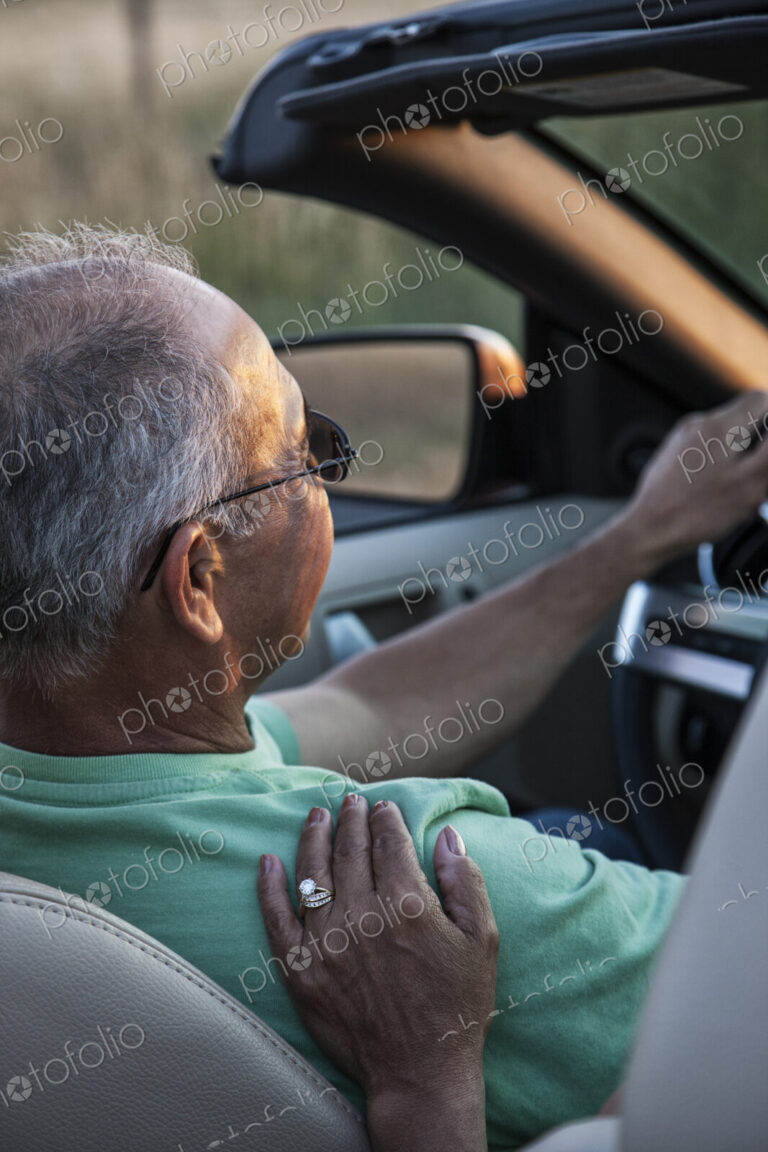 A closeup of a wife's hand on the shoulder of her husband driving a convertible sports…