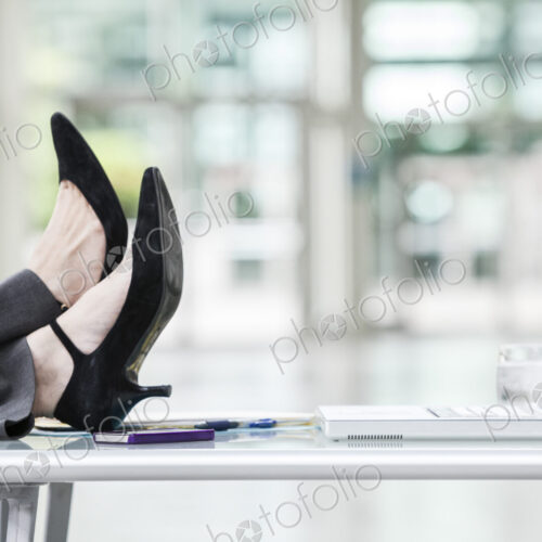 A closeup of feet and high heel shoes resting on a desk in front of a laptop computer. A closeup of feet and high heel shoes resting on a desk in front of a laptop computer.