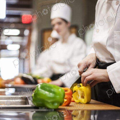 A closeup of the hands of a chef cutting vegetables in a commercial kitchen. A closeup of the hands of a chef cutting vegetables in a commercial kitchen.