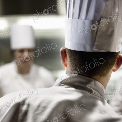 A closeup view from behind of a chef wearing a toque hat in a commercial kitchen.